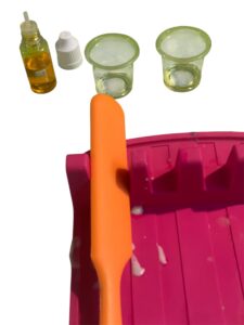 Gelbe Farbe mit zwei kleine mit Schaumkonzentrat und Duftöl gefüllten Likörgläsern, im Vordergrund ein orangener Spatel.